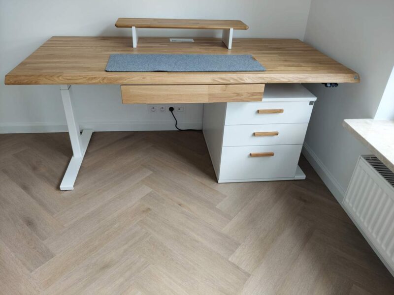 Verstellbarer Schreibtisch mit Holzplatte und weißem Sockel mit drei Schubladen