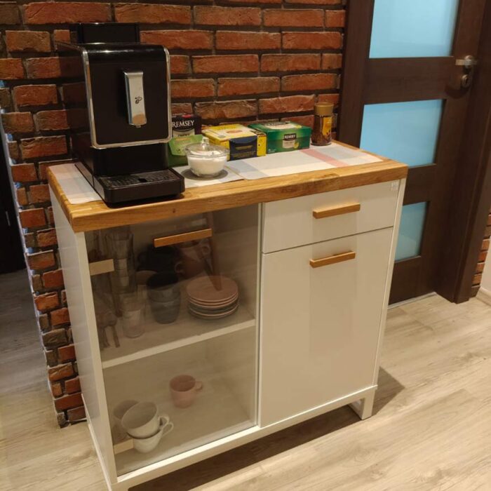 weißer Schrank mit einer Vitrine, auf der die Kaffeemaschine, Tee, Tassen und Gläser stehen