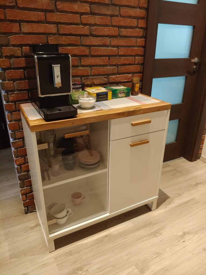 weißer Schrank mit einer Vitrine, auf der die Kaffeemaschine, Tee, Tassen und Gläser stehen